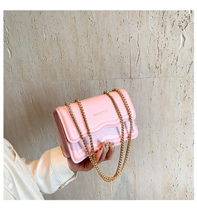 Close-up of a pink crossbody chain bag featuring a wavy flap and golden letter printing