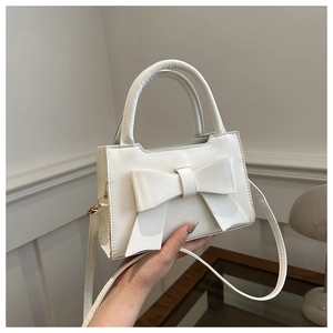 Detail of cream white handbag with large bow, round handle and gold hardware side view