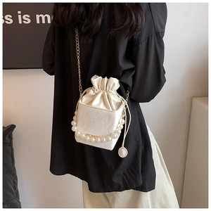 Detail of white satin drawstring bucket bag with large faux pearl handle and gold chain