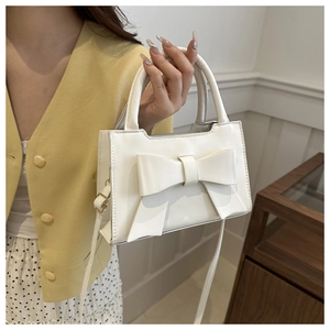 Detail of white handbag with a large bow held by a model in a bright interior setting
