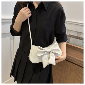 Detail of white patent leather shoulder bag with a large decorative bow and slim strap