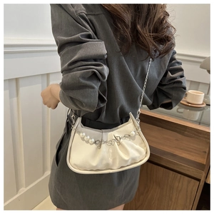 Close-up of a white pleated cloud bag featuring a pearl and floral metal chain detail