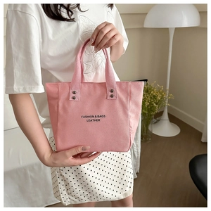 Detailed view of pink canvas tote bag with metal rivets and stylish black fashion lettering