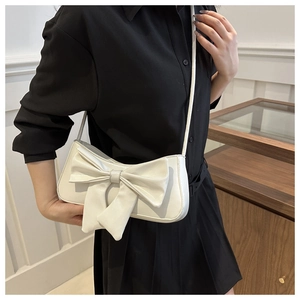 Detail of white crocodile texture bag with large bow and slim shoulder strap on model