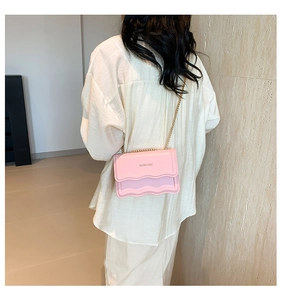Detail of light pink crossbody bag featuring scalloped edges and a gold chain strap