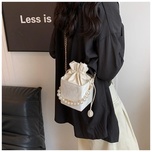 Detail of white drawstring bucket bag featuring pearl handle and gold chain strap
