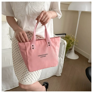 Détail du sac cabas en toile rose avec slogan noir et rivets métalliques sur l'anse