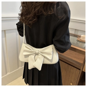 Detail of a creamy white underarm bag featuring a large decorative bow and glossy finish