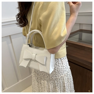 Side view of model wearing white bow handbag with adjustable crossbody strap