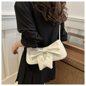 Close-up of white shoulder bag with large bow detail and glossy crocodile texture