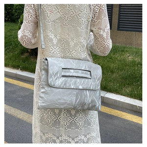 Detail of light gray pleated flap bag worn by a woman with an elegant white lace dress