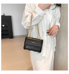 Detail of black leather crossbody bag featuring scallop edges and gold chain strap