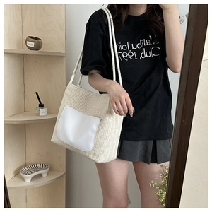 Detail of woven straw tote bag featuring a white leather pocket and stylish paper rope texture