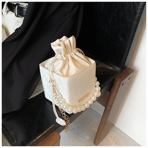 Detail of white satin bucket bag with pearl handle and golden chain on leather chair