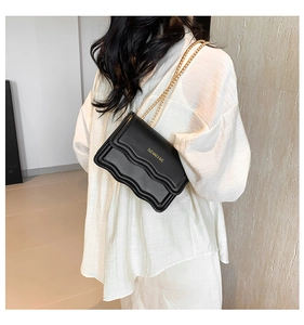 Close-up of black crossbody bag with wavy edges and golden chain strap on a model