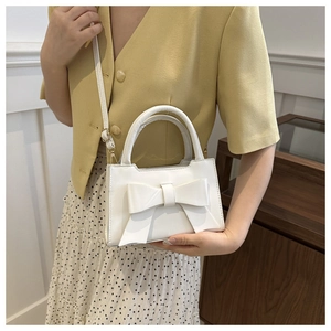 White mini square bag with a large bow detail shown on a model for casual styling