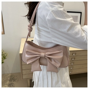 Close-up of pink glossy leather shoulder bag featuring a large decorative bow and knot strap
