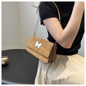 Close-up of brown quilted shoulder bag with silver butterfly buckle on a fashion model