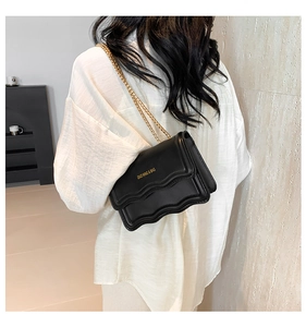 Detail of minimalist black crossbody bag with wavy flap and golden chain strap
