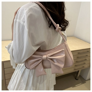 Pink shoulder bag featuring a large bow detail and crocodile texture on a model