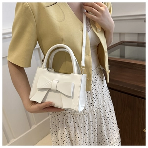 Detail of elegant cream handbag featuring a large bow and adjustable shoulder strap