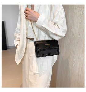 Detail of black wave pattern crossbody bag with gold chain strap on model shoulder