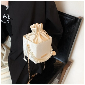 Close-up of white bucket bag with large pearl handle and gold chain strap detail