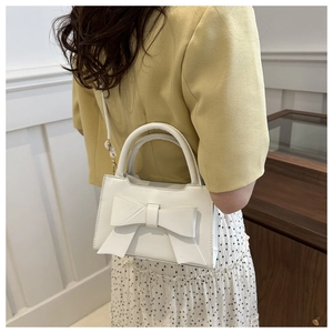 Detail of white mini crossbody bag with a large bow detail and matte leather finish