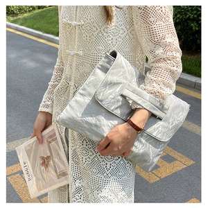 Close-up of metallic silver pleated clutch bag with handle cutout in outdoor setting