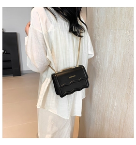 Macro detail of black leather crossbody bag with elegant wavy folds and gold chain strap