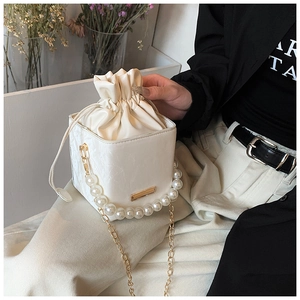 Detail view of a white drawstring bucket bag featuring pearl handle and gold chain strap