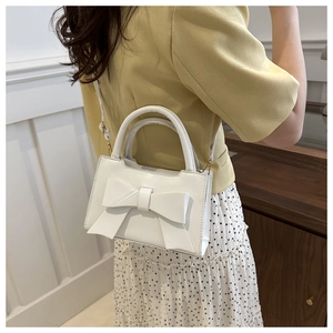 Detail of a white bow-knot crossbody bag held by a model in casual floral outfit