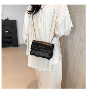 Detail of black crossbody bag featuring unique wave layered flap and slim gold chain strap