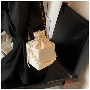 Detail of cream white bucket bag featuring luxury pearl handle and gold chain strap