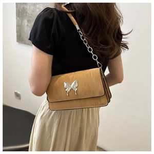 Caramel quilted shoulder bag with silver butterfly charm shown on model in a side view
