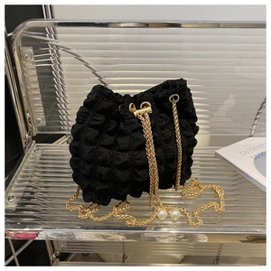 Dettaglio borsa a secchiello nera con texture popcorn, catena dorata e perle