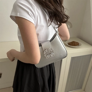 Silver metallic leather shoulder bag with rhinestone buckle shown on a female model