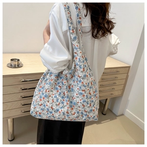 Rear view of a floral canvas tote bag with wide straps worn by a model in a minimal room