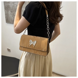 Close-up of caramel leather bag featuring a silver butterfly buckle and chain strap