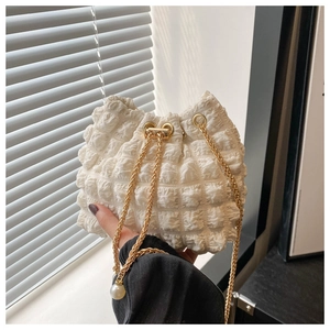 Dettaglio borsa a secchiello bianca con texture a bolle, catena oro e perla