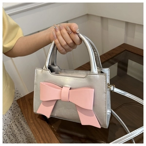 Detail of silver metallic handbag featuring a large pink bow and elegant round handle