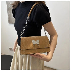 Detail of light brown patent leather bag featuring liquid silver butterfly ornament