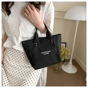 Detail of black canvas tote bag with fashion lettering and metal rivet reinforcements