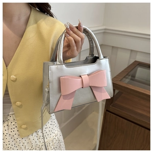 Detail of silver handbag with a large pink bow, featuring adjustable strap and handle