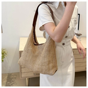 Detail view of woven straw tote bag with brown leather straps on a casual beige outfit