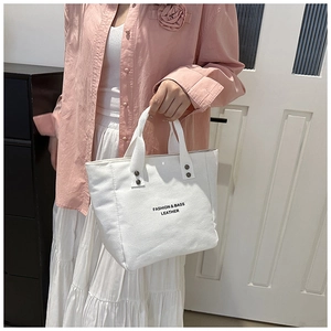 Detail of white canvas tote bag with reinforced silver rivets and black letter print