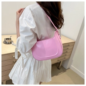 Pink patent leather underarm bag with a glossy finish shown on model shoulder