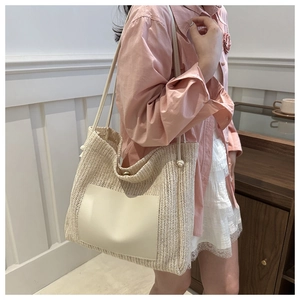 Detail of a beige woven straw tote bag with a leather pocket worn over the shoulder