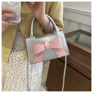 Close-up of metallic silver mini handbag with a large pink bow and slender strap