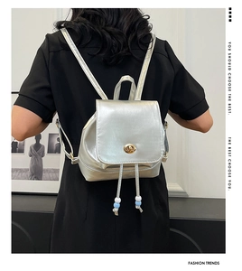 Detail of silver metallic mini backpack featuring a gold clasp and beaded drawstring cord